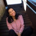 A Woman Sitting On A Bench Posing For The Camera